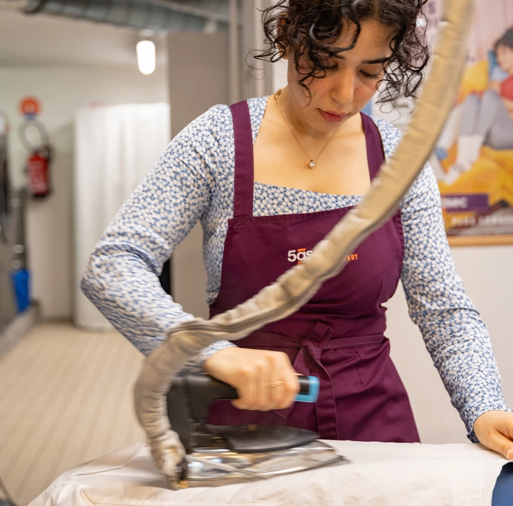Employée repassant un vêtement illustrant le processus nettoyage pressing en atelier