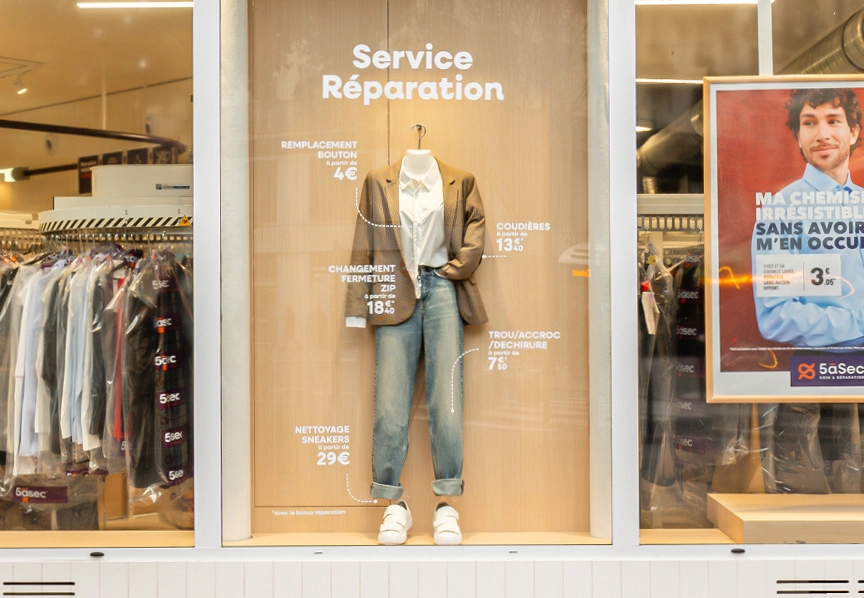 Vitrine de magasin présentant un service de réparation de vêtements dans une boutique du réseau franchise pressing 5asec spécialisée dans l’entretien textile.