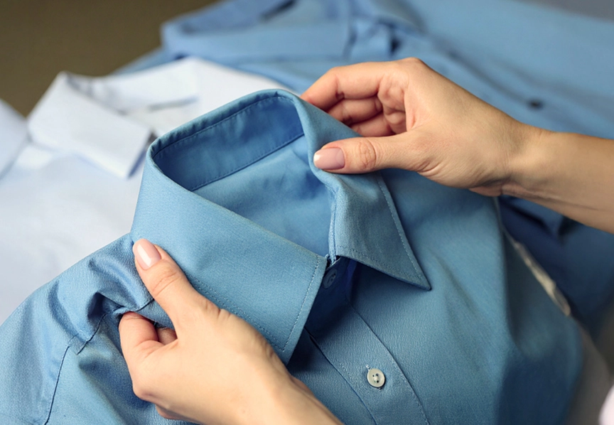 Une main tenant le col d'une chemise bleue pliée.