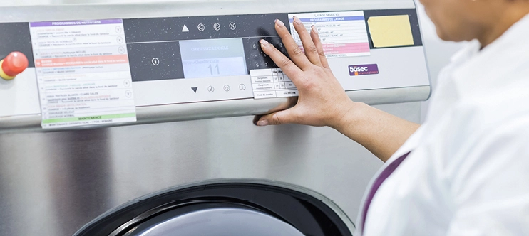 Technicienne utilisant une machine professionnelle pour le nettoyage ou lavage des vêtements